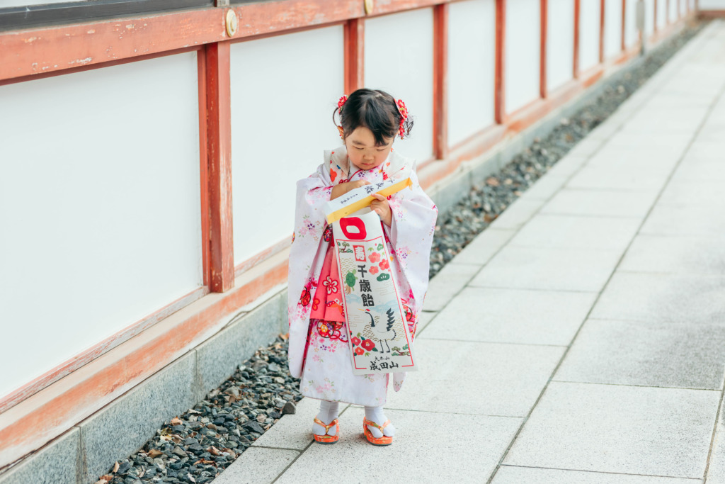 成田山新勝寺の聖徳太子堂付近で千歳飴の袋をのぞく七五三の女の子